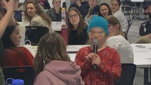 Young girl speaking to students using microphone.